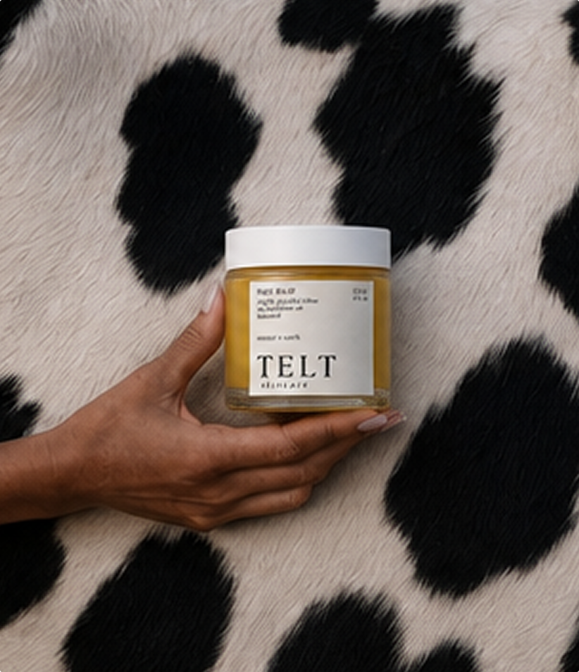 A hand holds a jar of Telt Deitach 'Pelt Balm' against a black and white cow-print faux fur background.